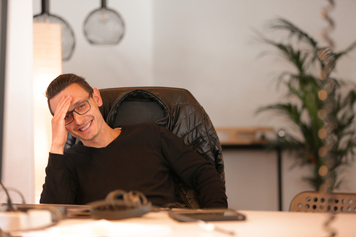 Ein Mitarbeiter am Schreibtisch schaut lächelnd in die Kamera.