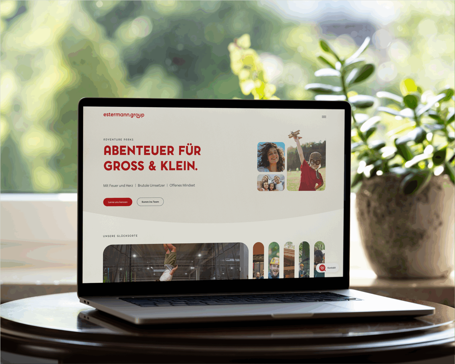 Ein Laptop auf einem Tisch mit Pflanzen im Hintergrund zeigt die Startseite der Estermann Website