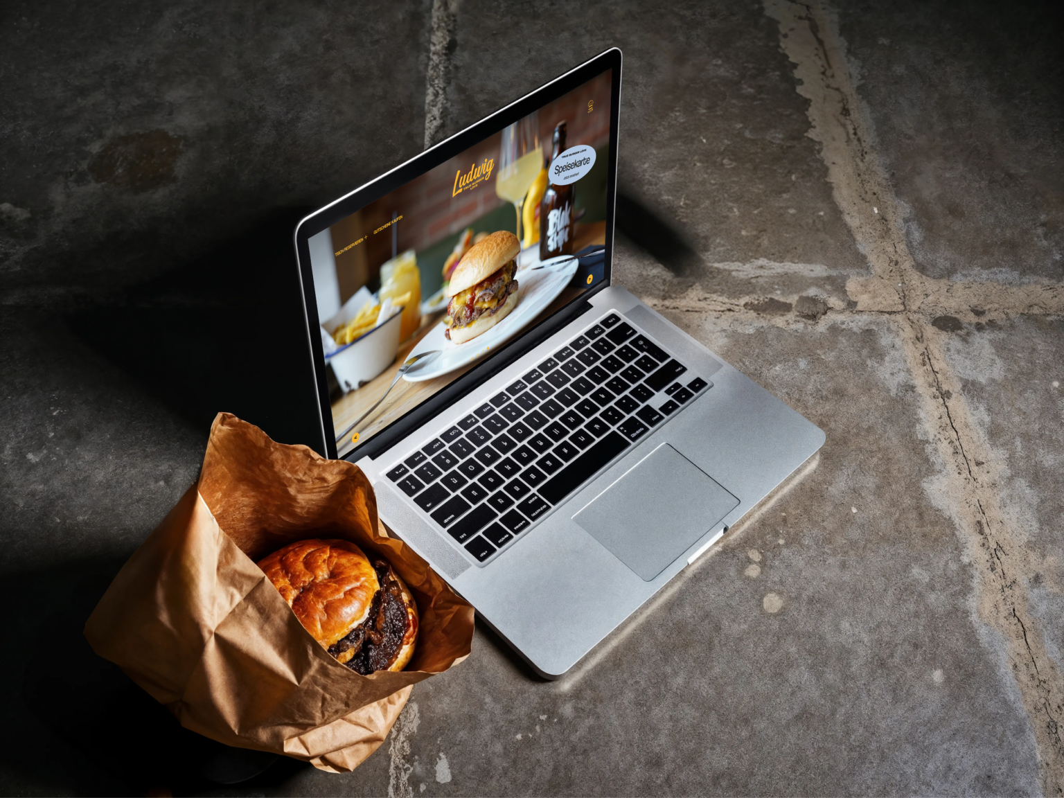 Ein Laptop der die Website von Ludwig Burger zeigt. Daneben liegt ein Burger.