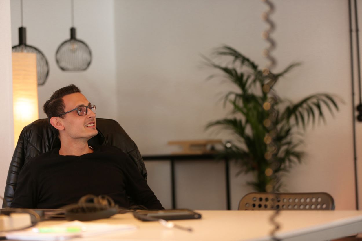 Rico sitzt entspannt im clubdrei Büro am Schreibtisch und lacht