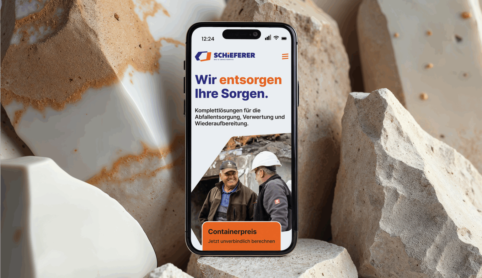 Ein Handy zeigt die Startseite von Schieferer und ist auf großen Steinen platziert